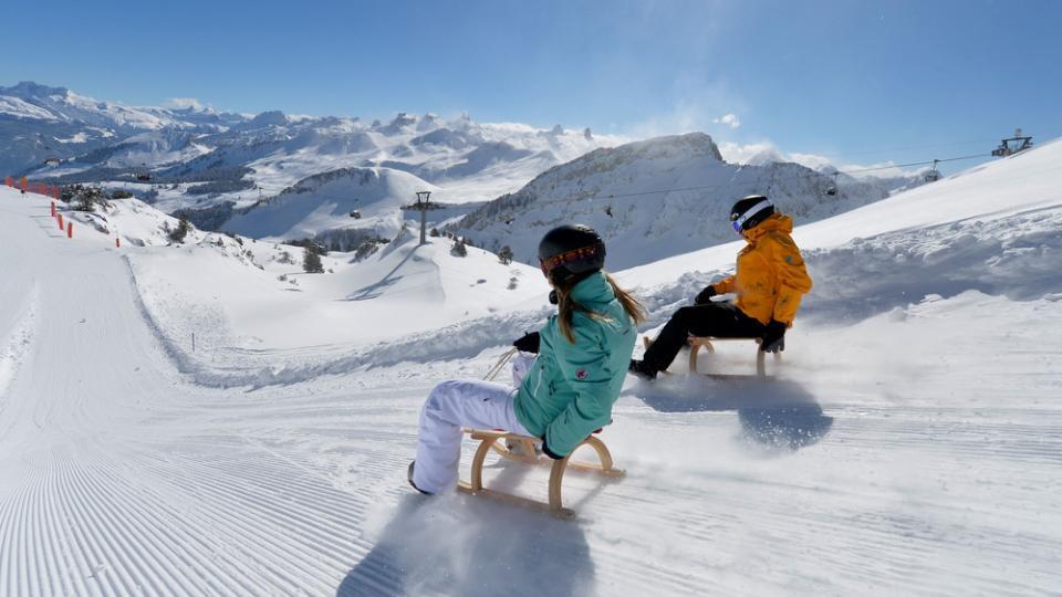 Rasante Schlittelabfahrt auf der frisch präparierten Strecke Richtung Stoos Dorf mit den verschneiten Bergen im Hintergrund.