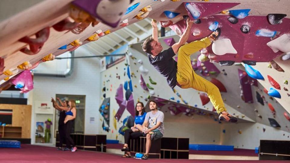 Mann beim Bouldern in der Boulder-Area Zug. Im Hintergrund schauen Personen zu.