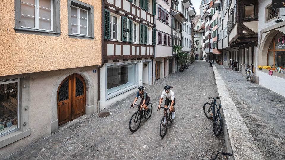 Zwei Gravelfahrende sind in der Zuger Altstadt unterwegs. Im Hintergrund ist der Zytturm sichtbar.